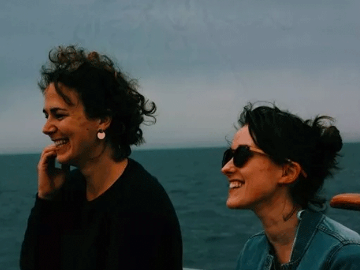 Women smile with the ocean behind them