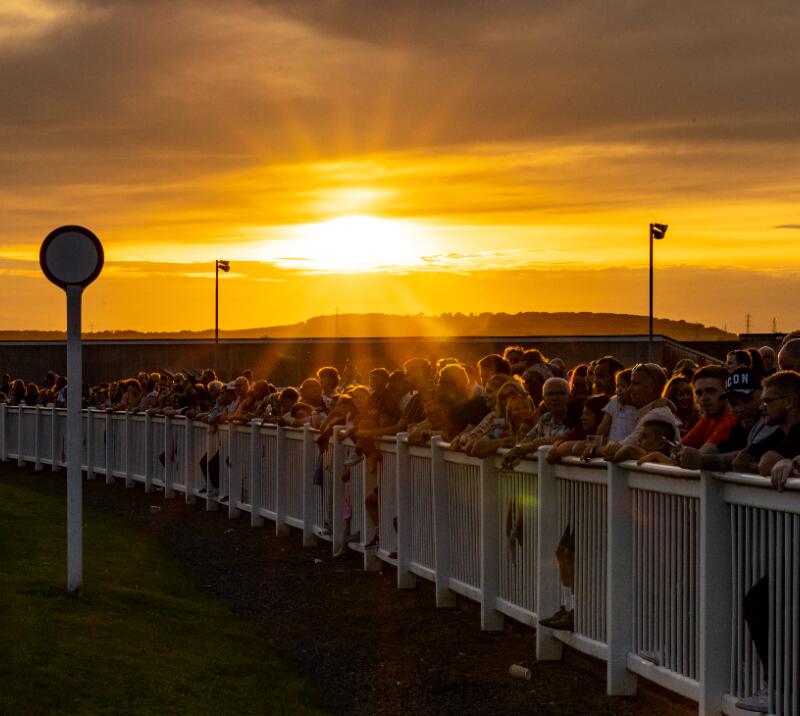 Sunset view of crowds lining up along the finishing straight at Ffos Las Racecourse