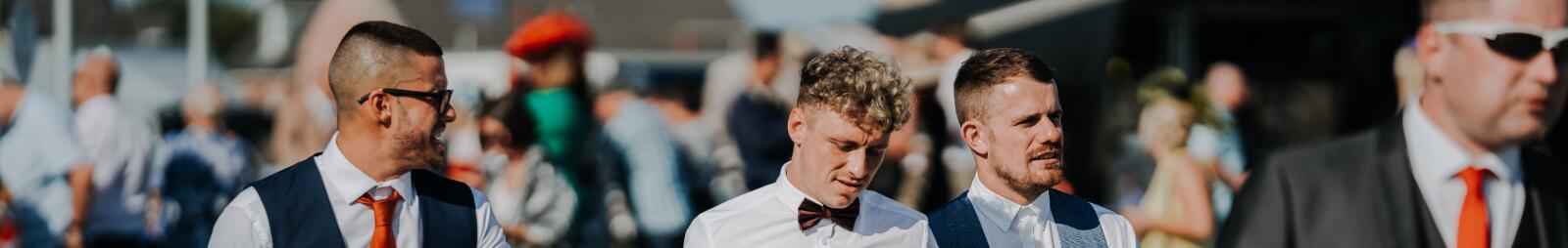 A group of guys dressed for the races walk across the racecourse