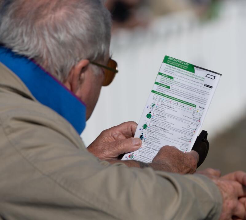 A close up of a race card over the shoulder of a visitor to Ffos Las Races