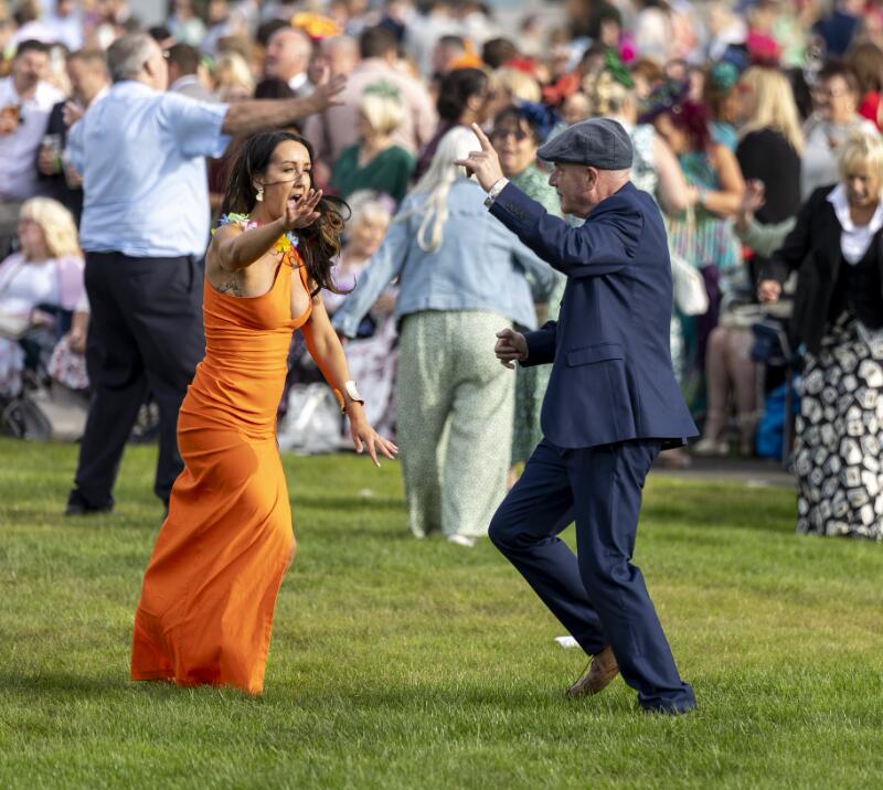 Two race goers dressed for the races dance together on the lawn at Ffos Las